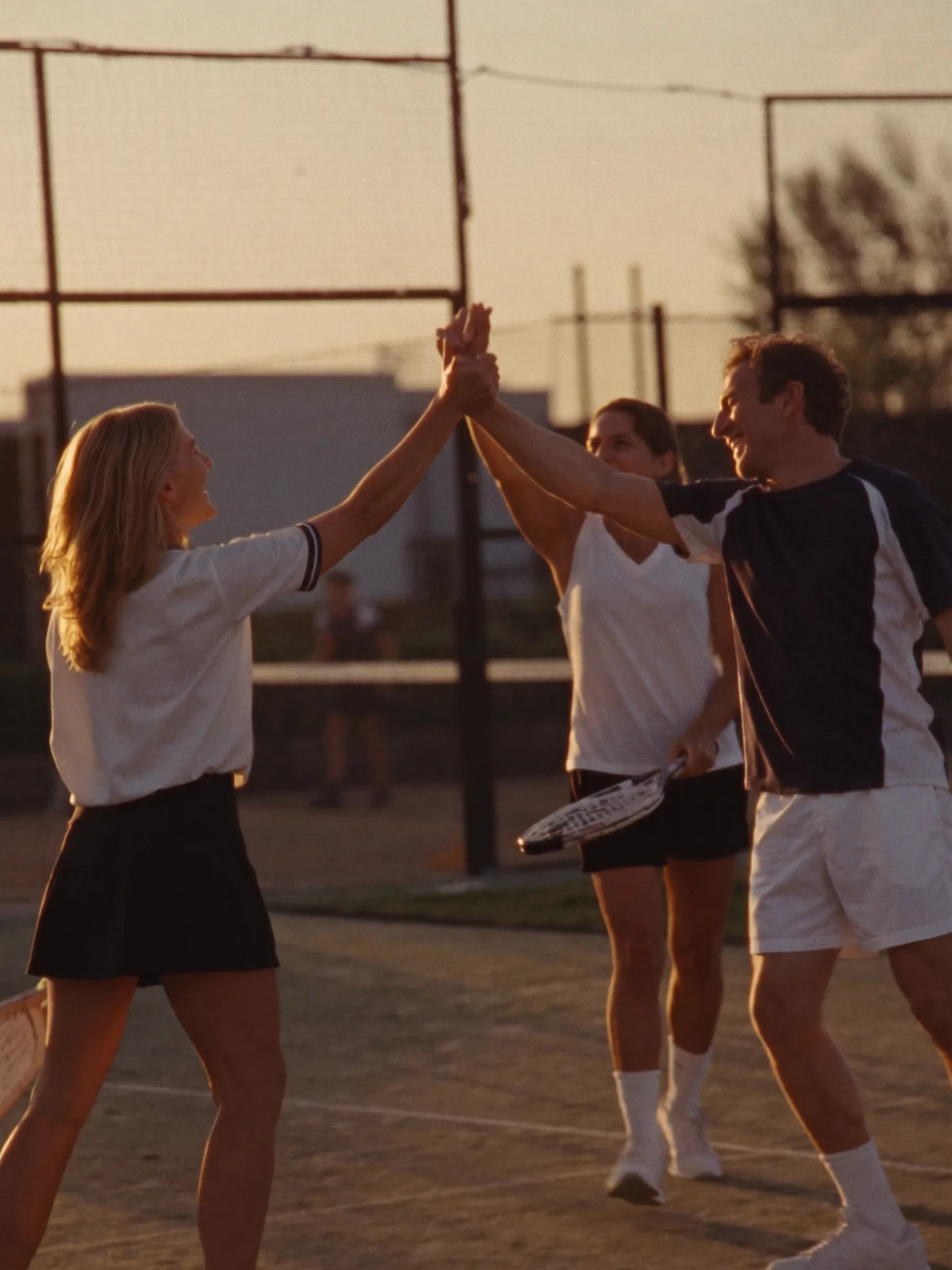 Friends high-fiving on a padel court at sunset