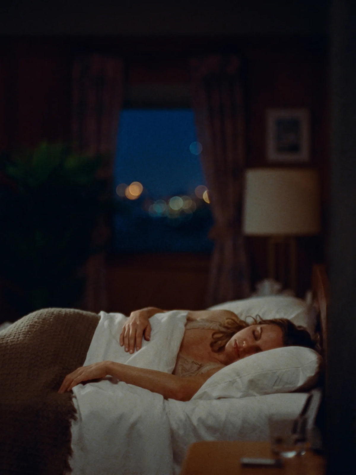Woman asleep in a dark bedroom, city lights in the window