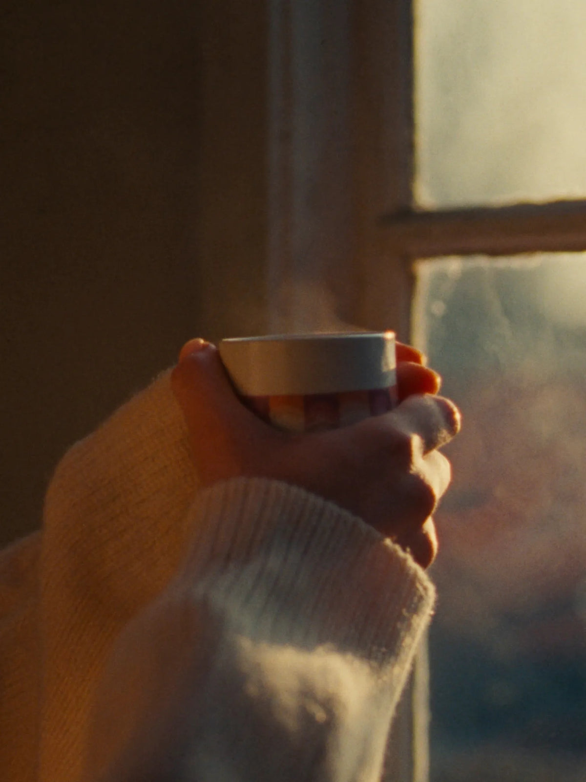 Hands around a warm mug in low winter sun by a frosted window
