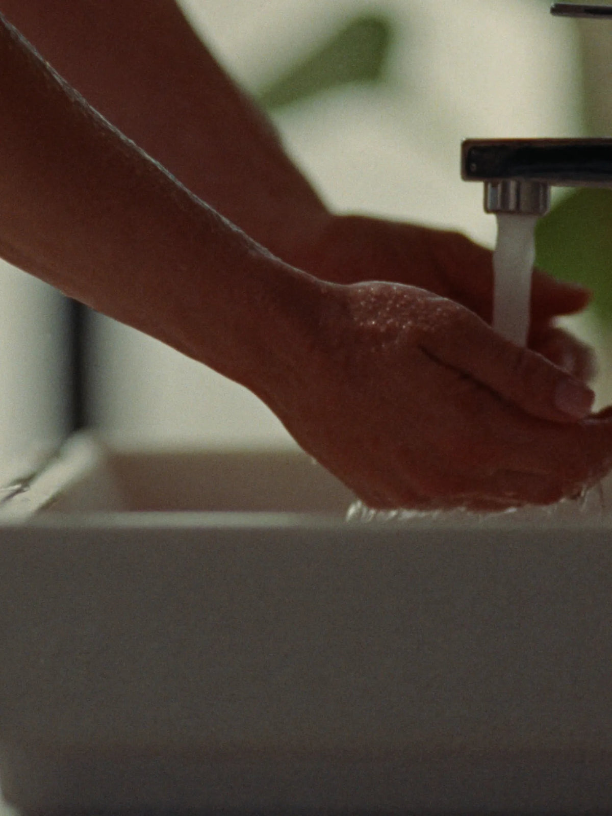 Hands under running water at a sink in morning sun